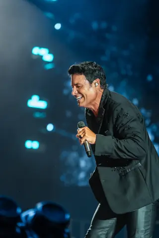 Chayanne canta con el micrófono en la mano bajo focos azules. Chayanne · Cook Music Fest, Tenerife, julio 2026