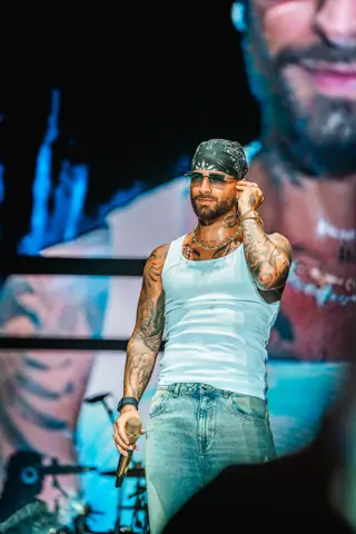 Maluma de camiseta blanca y pañuelo sobre el escenario, bajo luz azul. Maluma · Cook Music Fest, Tenerife, julio 2024