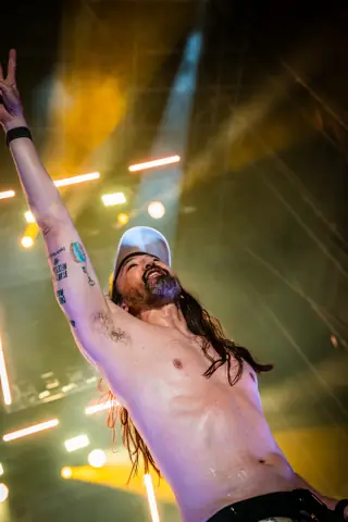 Steve Aoki con el brazo en alto y el torso desnudo bajo luz naranja. Lava Live, Lanzarote, julio 2025
