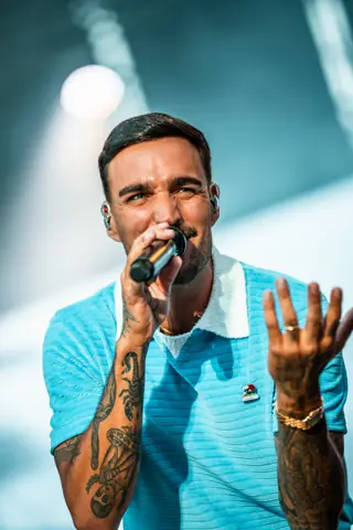 Rels B canta de cerca con polo azul y la mano abierta. Lava Live, Lanzarote, julio 2025