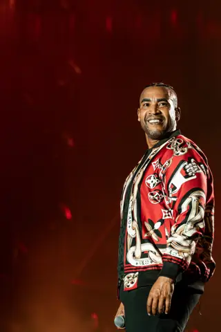 Don Omar sonríe con chaqueta roja estampada bajo luz cálida. Cook Music Fest, Tenerife, julio 2026.