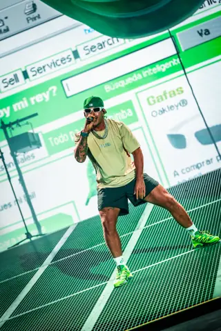Feid sings in white glasses and a green cap before a green screen. Granca Live Fest, Gran Canaria, July 2025. Photo for Why Agency.