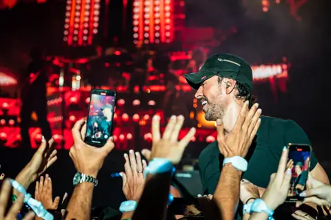Enrique Iglesias in profile, in a cap, among the crowd and red lights. Granca Live Fest, Gran Canaria, July 2025. Photo for Why Agency.