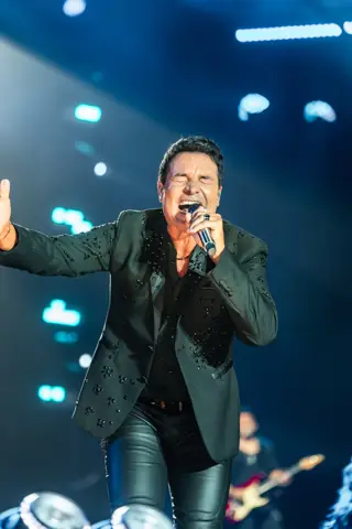 Chayanne canta al micrófono con el brazo extendido bajo luz azul. Cook Music Fest, Tenerife, julio 2026.