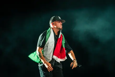Residente con la bandera al hombro entre humo verde. Lava Live, Lanzarote, junio 2025. Foto para Why Agency.