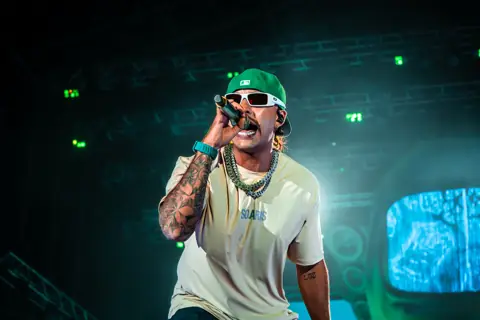 Feid up close, in white glasses and a green cap, singing into the mic. Granca Live Fest, Gran Canaria, July 2025. Photo for Why Agency.