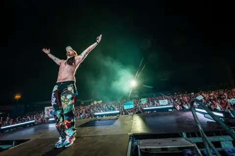 Steve Aoki abre los brazos ante el público entre humo verde. Lava Live, Lanzarote, julio 2025. Foto para Why Agency.