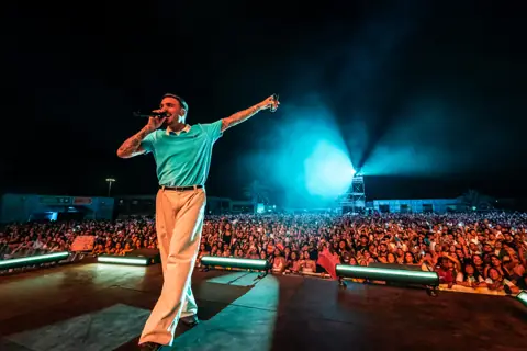 Rels B señala al cielo ante una multitud de noche. Lava Live, Lanzarote, julio 2025. Foto para Why Agency.