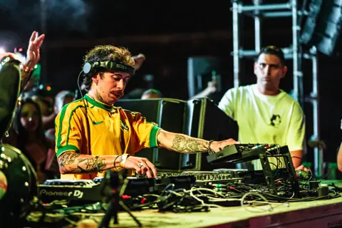 Mochakk DJing in the Brazil jersey. Sun Paradise Oasis, Tenerife, June 2024. Photo for Okidoki.