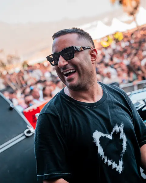Joseph Capriati smiles in sunglasses at the decks, with the sunlit crowd behind. Sunblast, Tenerife, August 2024. Photo for Esther Bronchal (DJ).