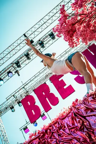 Bailarina sobre una tarima de tela rosa metalizada bajo letras gigantes. Bresh, Tenerife, mayo 2025
