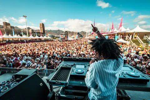 Renzzo señala al cielo desde la cabina, con el público y las montañas. Cook Music Fest, Tenerife, julio 2025