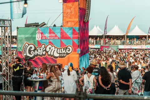 Público, gradas y carpas blancas junto al escenario al atardecer. Cook Music Fest, Tenerife, julio 2026