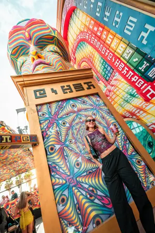 Asistente posa ante un panel psicodélico bajo la cabeza gigante. elrow Tenerife, octubre 2025