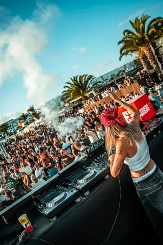 DJ con pañuelo rojo, de espaldas en la cabina, ante público y palmeras. EMEC Lanzarote, mayo 2025