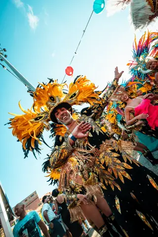 Bailarín con tocado de plumas doradas saluda en el desfile de día. La Santa (Tropicalia), Tenerife, agosto 2025