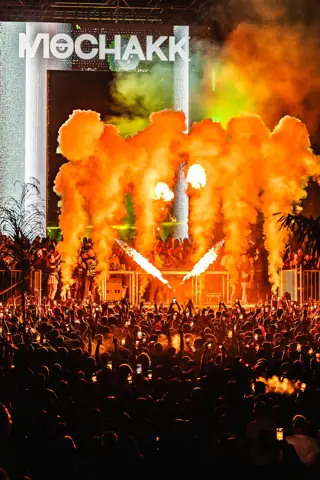Llamas y humo naranja ante la cabina de Mochakk y miles de móviles. Mochakk · Sun Paradise Oasis, Tenerife, junio 2024