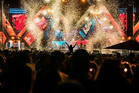 Silueta con brazos en alto bajo lluvia de confeti y coches sobre el escenario. Love Reggaeton, Madrid, junio 2024