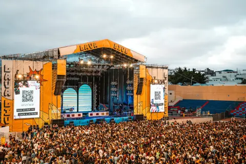 Escenario del concierto de Camilo en la Ciudad Deportiva de Lanzarote, con sus pantallas y el público bajo cielo gris. Camilo, Lanzarote, junio 2024