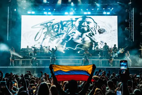 Bandera de Colombia entre el público ante un escenario con bailarinas. Lava Live, Lanzarote, julio 2024
