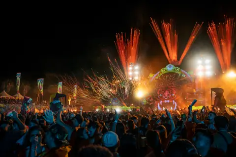 Pirotecnia sobre el escenario de elrow y el público con los brazos en alto, de noche. elrow Tenerife XXL, octubre 2026