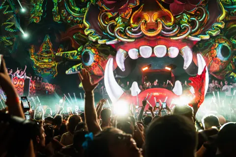 Fauces gigantes de la escenografía sobre la cabina y el público con las manos en alto. elrow Tenerife XXL, octubre 2026