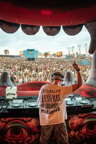 DJ con los brazos abiertos en la cabina ante un mar de público de día. elrow Tenerife XXL, octubre 2026
