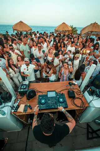 DJ pincha en una terraza llena frente al mar al atardecer. Noor (Riela), Tenerife, agosto 2025