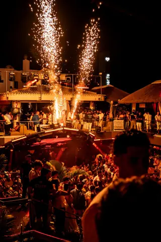 Chispas de fuego frío sobre la terraza llena y los tejados de paja. Tribu Beach, Tenerife, agosto 2026