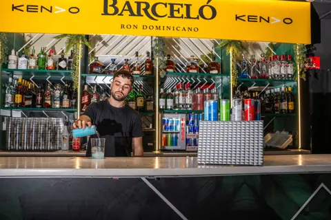 Camarero sirve una lata de Red Bull en la barra, con nevera de marca. Red Bull × Kendo, Tenerife, diciembre 2025