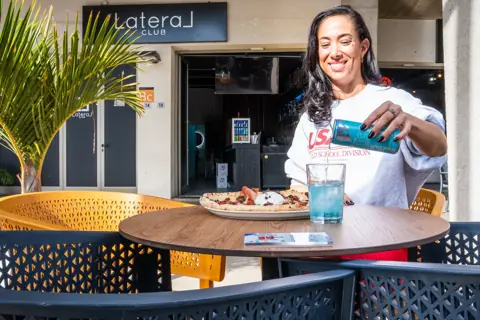 Mujer sirve una lata de Red Bull junto a una pizza en terraza. Red Bull × Lateral Club, Tenerife, diciembre 2025